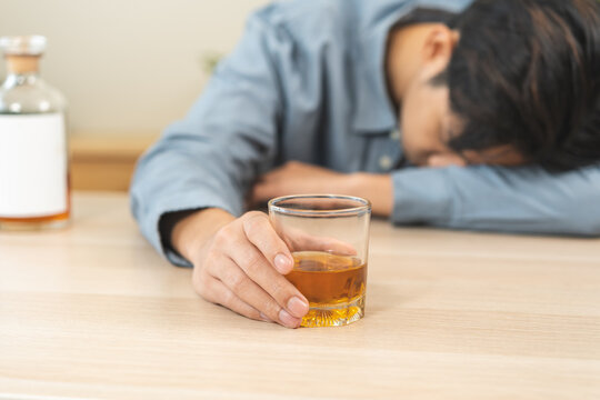 Health care alcoholism drunk, fatigue asian young man hand holding glass of whiskey, alone depressed male drink booze on sofa at home. Treatment of alcohol addiction, suffer abuse problem alcoholism.