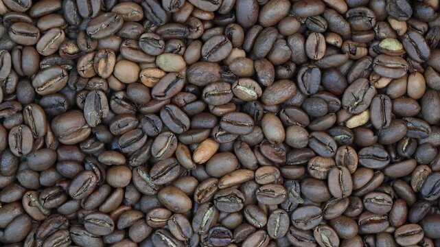 Close up rotating top view of freshly roasted coffee beans forming a rich dark textured background