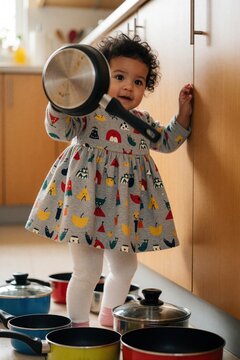 Little child plays with kitchenware on floor in home. Toddler girl in dress has fun with pots and pans making noise, exploring her environment.