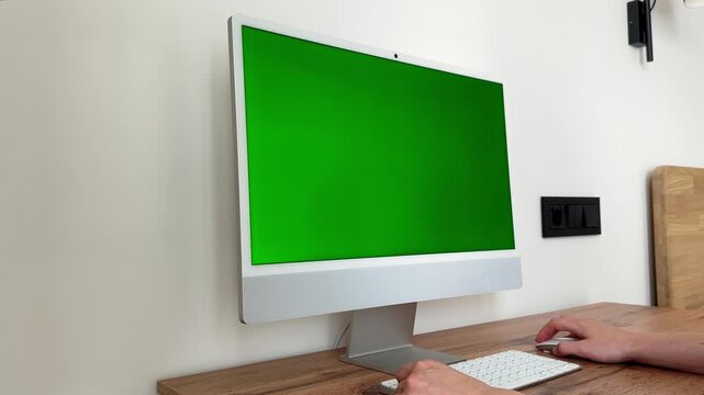 green screen mockup running on digital workstation display. Operator hand clicking hardware mouse triggers custom software layout changes over wooden desk. Bright remote home office