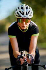 Naklejka premium Female Cyclist Training on Road Bike Wearing Helmet and Mirrored Sunglasses in Aerodynamic Position