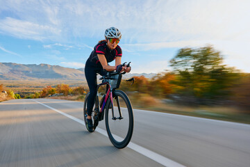 Naklejka premium Female Cyclist Speeding on Road Bike Through Autumn Mountains During Time Trial Training