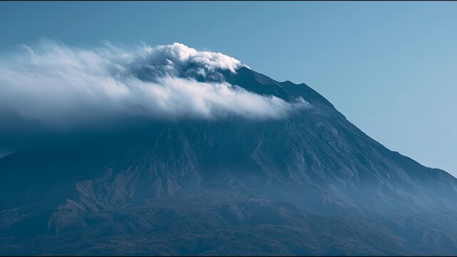 Majestic mountain peak covered by dramatic clouds under blue sky