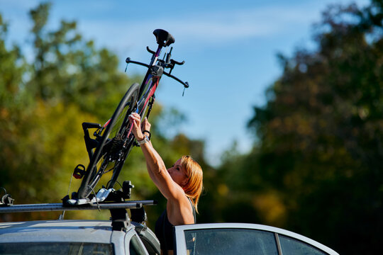 Woman Loading Bicycle Onto Car Roof Rack Outdoors Before Road Ride