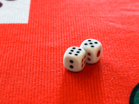 Close-up of two white dice resting on a vibrant red textured gaming mat, highlighting a lucky roll for a board game or casino play.