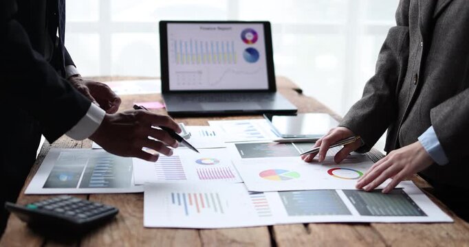 Business professionals analyzing financial data using a calculator and laptop with charts, collaborating on a marketing strategy in an office workspace