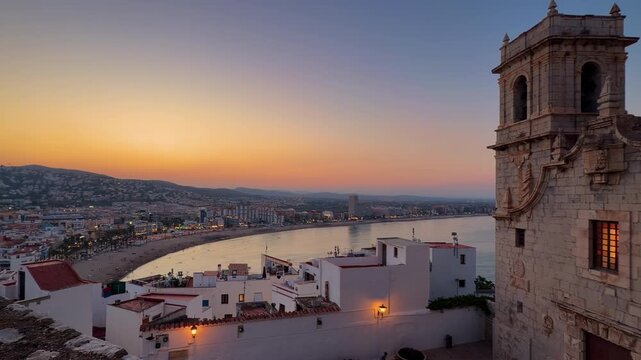 Peniscola beach and church tower at dusk view, Castellon Spain. Mediterranean coastline, illuminated old town white houses and sunset sky. High quality 4k footage