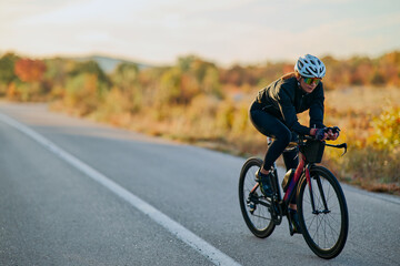 Fototapeta premium Female Cyclist Training on Road Bike at Sunrise in Autumn Countryside Cycling Fitness and Speed