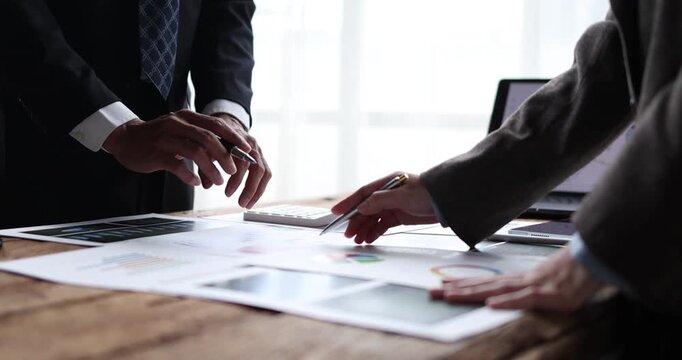 Business team analyzing financial reports and charts at a wooden table, pointing at a laptop screen, calculating figures on a calculator and planning growth strategy together