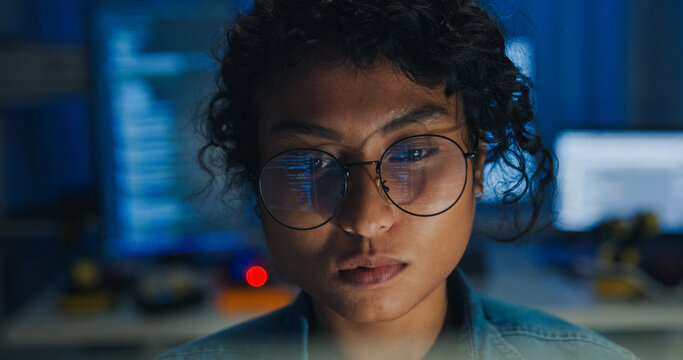 Close-up Black female programmer with code reflection in glasses working late in home office at night. Cybersecurity, AI algorithm, Network security, software developer, serious face, burnout concept.