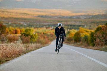 Naklejka premium Road Cyclist Training On Scenic Autumn Highway At Sunrise Fitness Cycling Athlete Outdoor Endurance