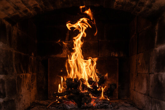 Bright flame rising from glowing embers in stone fireplace