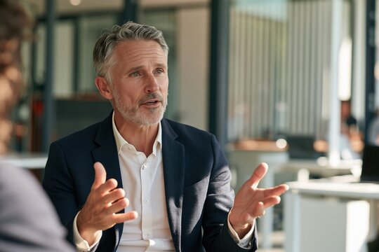 Professional middle aged man speaking with expressive hand gestures in office meeting for corporate discussion and presentation background