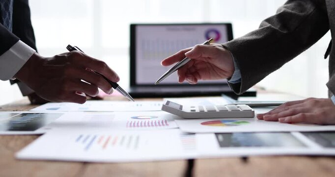 Business team analyzing financial reports and charts at a wooden table, pointing at a laptop screen, calculating figures on a calculator and planning growth strategy together