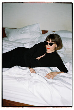 An elegant woman in a black dress lies on a bed