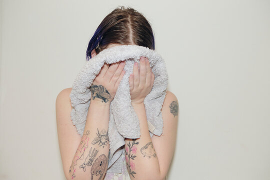 Tattooed person drying their face with a towel
