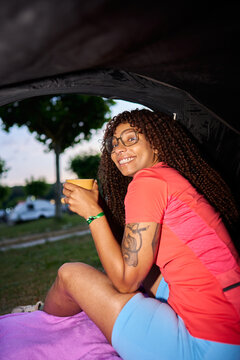 Woman enjoying drink while relaxing at campsite tent