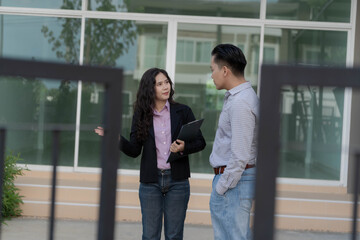 Fototapeta premium Female real estate agent showing new townhouse property to male buyer outdoor