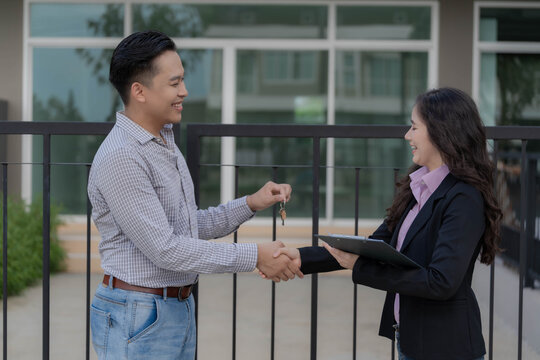 Female real estate agent handing house keys to young male customer in front of new property