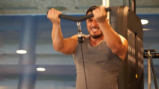 Athletic man doing tricep cable pushdowns with V-bar attachment with intense effort in a modern gym interior