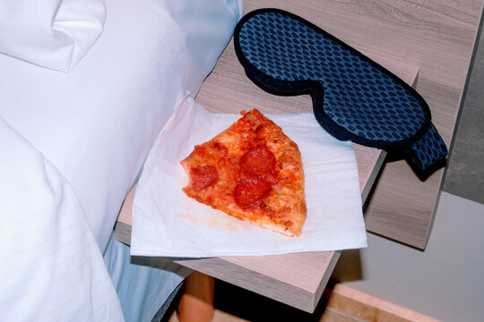 a close-up of pepperoni pizza and a sleep mask beside a bed