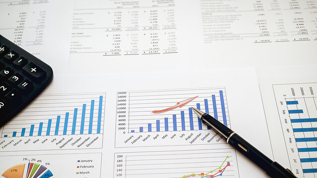 A professional financial analysis scene showing business growth charts with a calculator and a black pen on a desktop, captured in a high-angle shot (b 84)