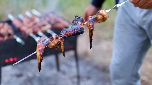 Step by step preparation of chicken wings seasoned with salt and pepper, mixed with onion, marinated and grilled on metal skewers over hot charcoal for an outdoor barbecue. Close up.