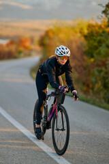 Naklejka premium Female Cyclist Training On A Road Bike At Sunrise Through Autumn Countryside