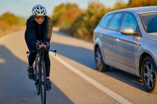 Female Cyclist Riding a Road Bike Alongside a Passing Car on a Country Road in Autumn