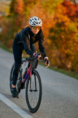 Fototapeta premium Female Cyclist Training on Road Bike During Autumn Golden Hour Ride