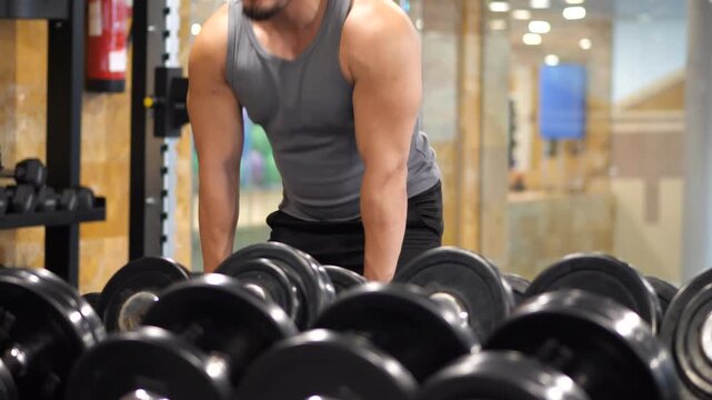 Muscular man picking up heavy dumbbells from a weight rack for a strength training session in a modern indoor gym setting