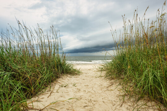 Cloudy sky over sandy path leading to water at the beach