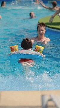 Little boy swimming with inflatable ring and armbands towards mother in pool