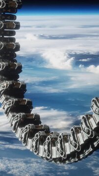 A circular structure is floating in space above Earth. Below, clouds and blue water are visible. The scene shows the vastness of outer space. The location is high above the planet.