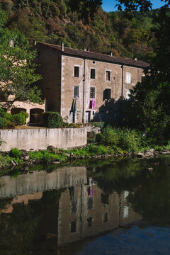 Old stone house reflected in a calm river with laundry hanging outside