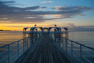 Fototapeta premium A metal pier set against the backdrop of a picturesque sunrise over Lake Issyk-Kul, near the Kyrgyz city of Cholpon-Ata.