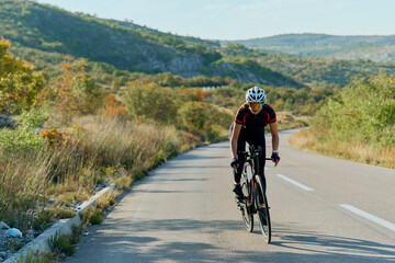 Fototapeta premium Road Cyclist Training on Scenic Rural Highway Surrounded by Hills and Autumn Vegetation