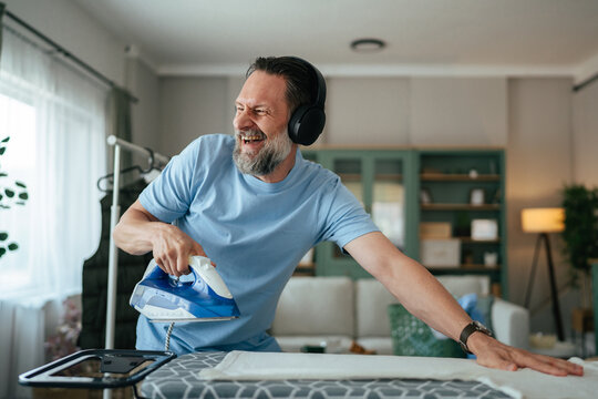 Happy man ironing while listening to music with headphones