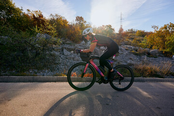 Naklejka premium Female Cyclist Training On Road Bike During Autumn Ride Through Rocky Countryside