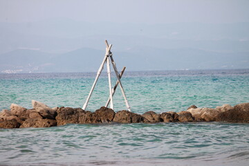 Handmade wooden tripod structure on a rocky sea shore with turquoise water © Ljiljana