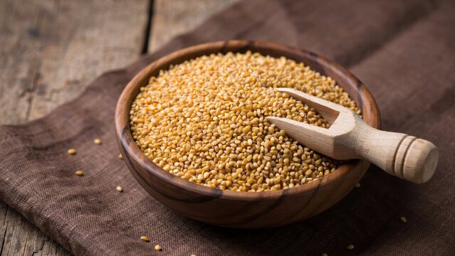Bowl of raw bulgur wheat grains with a wooden scoop on a rustic dark wooden background.