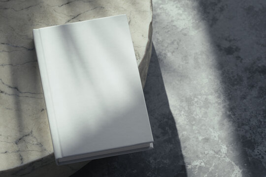 Minimalist 3D render of a blank white hardcover book lying on a round beige marble table with a rough raw edge, soft natural sunlight, botanical window gobo shadow and copy space for book cover mockup