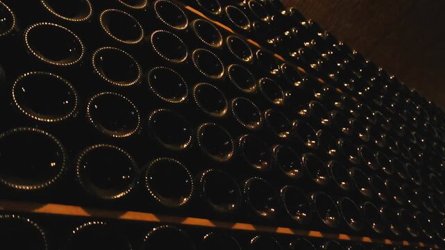 Rows Of Stacked Glass Wine Bottles In Dark Cellar With Warm Lighting