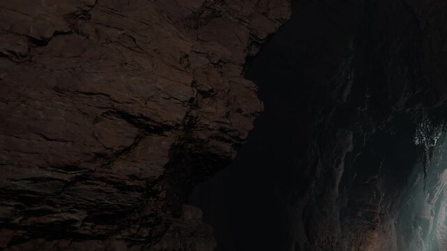 In a dark cave, rocky walls are visible. A hint of water can be seen reflecting light in the distance. The atmosphere indicates a hidden and unexplored area within the cave.