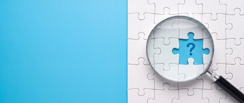 Magnifying glass over a missing white puzzle piece with jigsaw puzzle reveals piece marked question positioned over gap reveals single blue investigation uncertainty