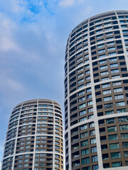 Fototapeta premium Tall buildings under a cloudy sky. Two tall buildings stand against a cloudy sky. The setting shows urban architecture with many windows.