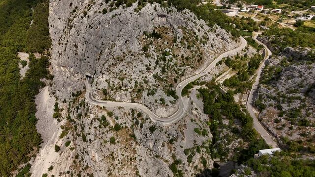 Dynamic aerial drone flight following a winding mountain road through the Croatian countryside, with sharp bends, rocky hills and lush green Mediterranean scenery.