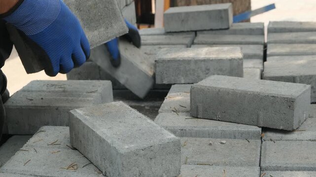 Construction workers hands stacking gray bricks from a pallet, bricklaying and wall construction, mason in blue gloves at work, masonry construction, building materials, skilled manual labor