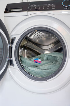 Laundry detergent pod placed on towel inside open front loading washing machine
