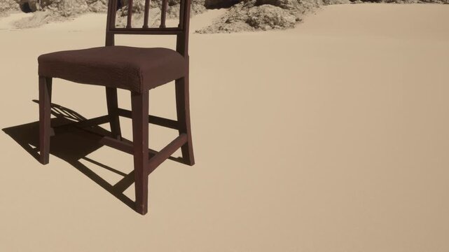 A wooden chair stands alone on a sandy area surrounded by rocks. The setting appears isolated and quiet, showing no other objects or people nearby.